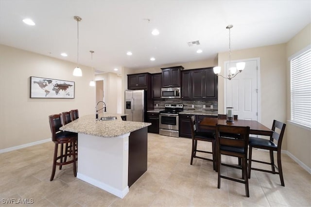 kitchen with appliances with stainless steel finishes, a kitchen breakfast bar, decorative light fixtures, and a kitchen island with sink