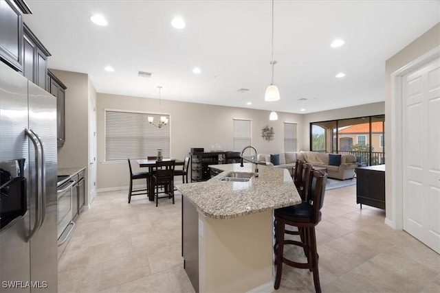 kitchen with an island with sink, sink, a kitchen breakfast bar, hanging light fixtures, and stainless steel appliances