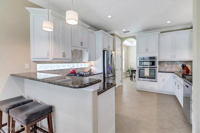 kitchen with pendant lighting, white cabinets, appliances with stainless steel finishes, kitchen peninsula, and a breakfast bar area