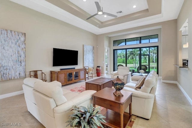 living room with a tray ceiling, ceiling fan, a towering ceiling, and light tile patterned flooring