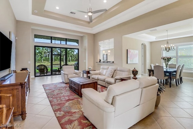 tiled living room with a towering ceiling, ceiling fan with notable chandelier, a tray ceiling, and a wealth of natural light