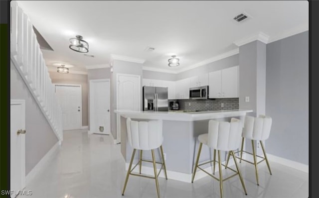 kitchen featuring tasteful backsplash, ornamental molding, stainless steel appliances, a breakfast bar, and white cabinets