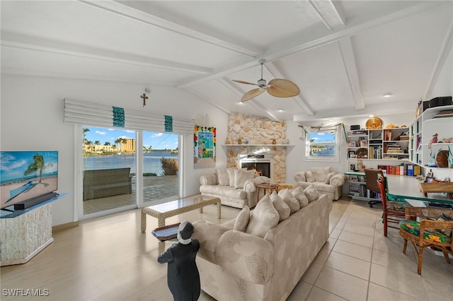 living room with ceiling fan, a stone fireplace, light hardwood / wood-style flooring, lofted ceiling with beams, and a water view