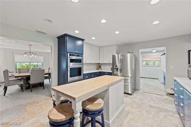 kitchen with blue cabinetry, stainless steel appliances, backsplash, decorative light fixtures, and white cabinets