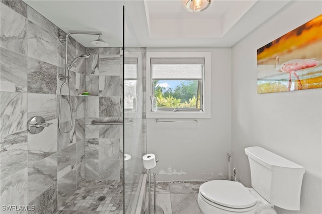 bathroom with toilet, a tile shower, and a tray ceiling