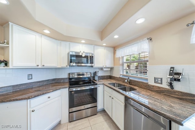 kitchen with sink, appliances with stainless steel finishes, dark stone countertops, light tile patterned floors, and white cabinets