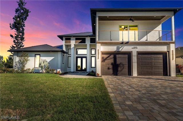 modern home with a lawn, ceiling fan, french doors, a balcony, and a garage