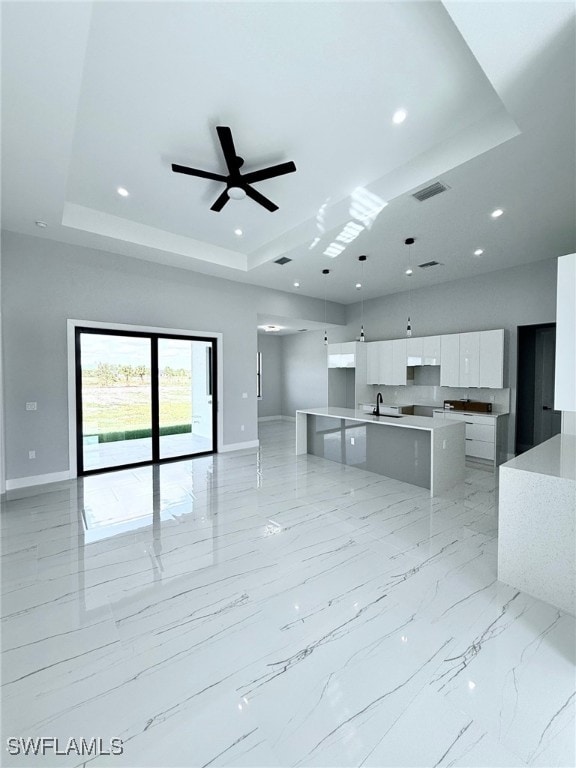 unfurnished living room with a raised ceiling, ceiling fan, and sink