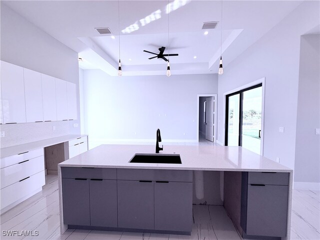 kitchen with ceiling fan, sink, hanging light fixtures, a raised ceiling, and a large island with sink