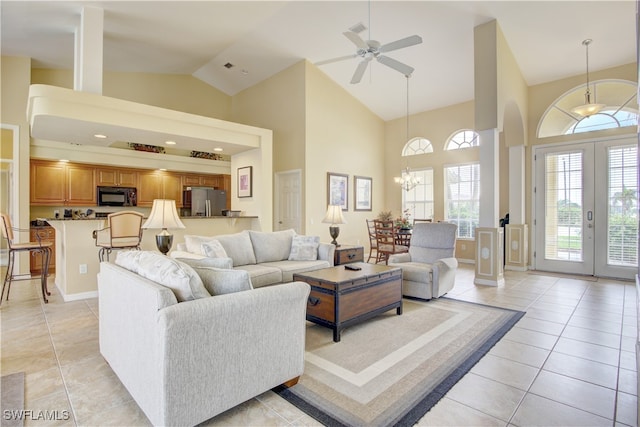 tiled living room featuring high vaulted ceiling, french doors, and ceiling fan with notable chandelier