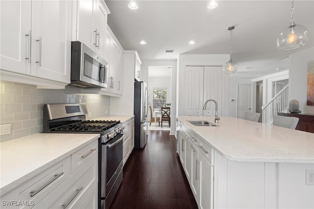 kitchen featuring a center island with sink, sink, appliances with stainless steel finishes, decorative light fixtures, and white cabinetry