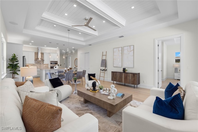 living room featuring ceiling fan with notable chandelier, light hardwood / wood-style floors, and a raised ceiling