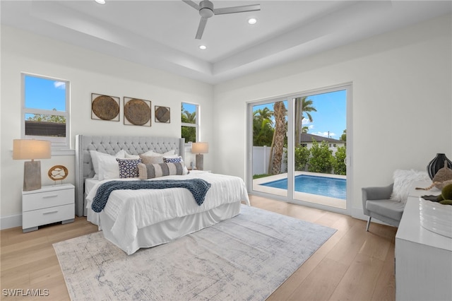 bedroom featuring a tray ceiling, access to outside, multiple windows, light wood finished floors, and recessed lighting