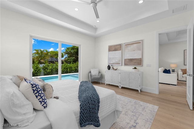 bedroom with access to outside, ceiling fan, a tray ceiling, and light wood-type flooring