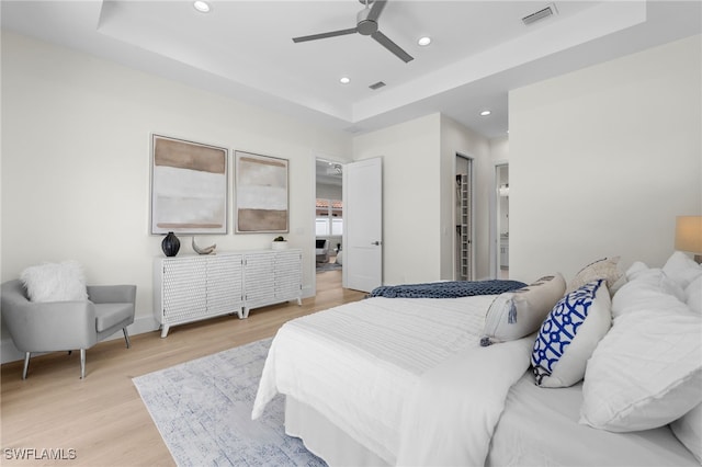 bedroom with a raised ceiling, recessed lighting, light wood-style floors, a ceiling fan, and baseboards