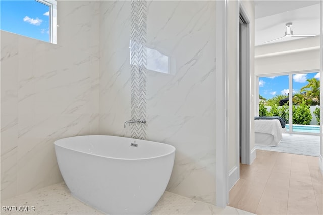 bathroom featuring a bathing tub, a healthy amount of sunlight, and tile walls