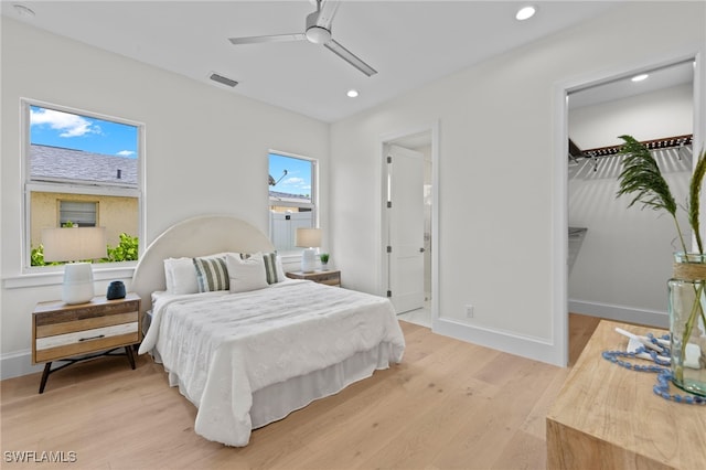 bedroom featuring ceiling fan, a walk in closet, light wood-type flooring, and multiple windows