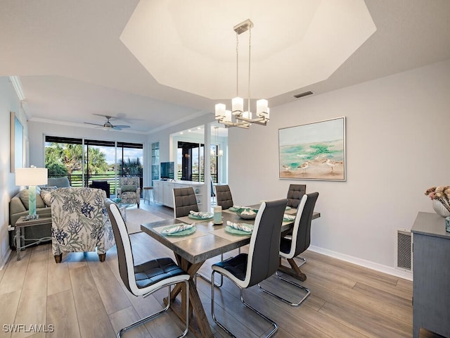 dining space with ornamental molding, a raised ceiling, ceiling fan with notable chandelier, and light hardwood / wood-style flooring