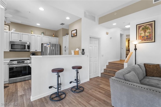 kitchen featuring appliances with stainless steel finishes, a kitchen breakfast bar, light hardwood / wood-style floors, white cabinets, and kitchen peninsula