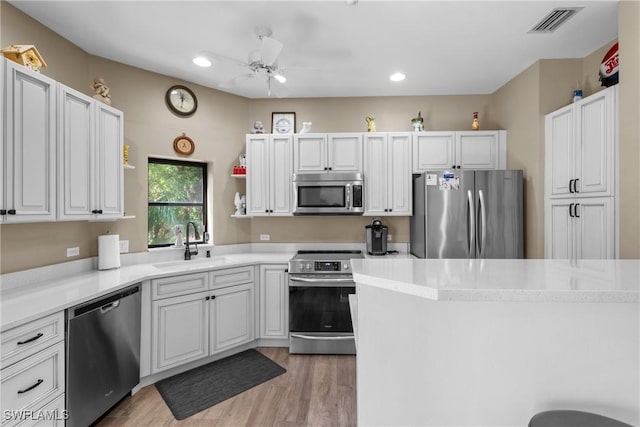 kitchen featuring sink, ceiling fan, stainless steel appliances, white cabinets, and light wood-type flooring