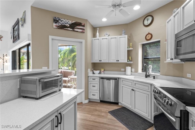 kitchen with appliances with stainless steel finishes, white cabinetry, sink, ceiling fan, and light hardwood / wood-style flooring