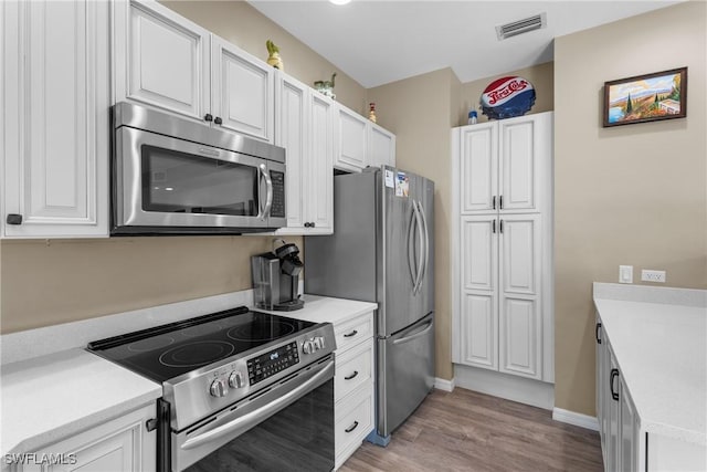 kitchen with stainless steel appliances, light hardwood / wood-style floors, and white cabinets