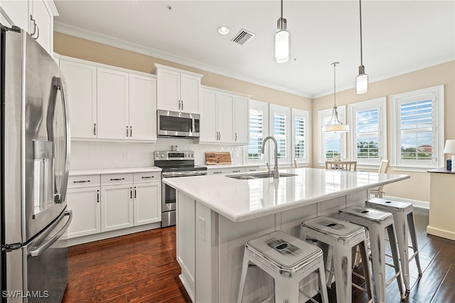 kitchen with stainless steel appliances, dark wood-type flooring, a center island with sink, white cabinets, and decorative light fixtures