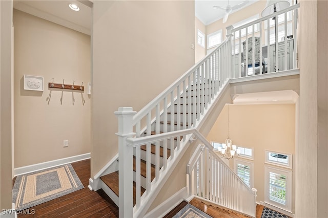 staircase featuring ceiling fan with notable chandelier, hardwood / wood-style flooring, crown molding, and a towering ceiling