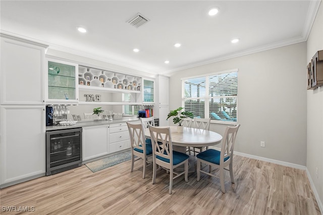 dining area with beverage cooler, crown molding, light hardwood / wood-style flooring, and bar area