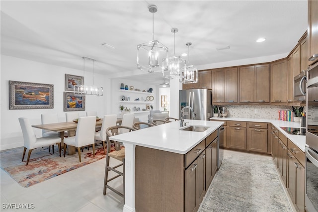 kitchen with stainless steel appliances, a center island with sink, sink, a kitchen breakfast bar, and decorative light fixtures