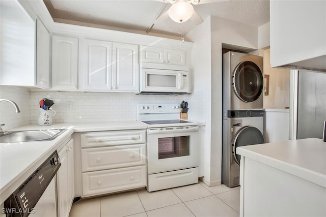 kitchen featuring white appliances, sink, light tile patterned floors, white cabinets, and stacked washer / drying machine