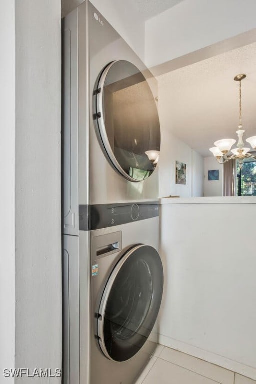 laundry room featuring tile patterned floors, stacked washer / drying machine, and an inviting chandelier