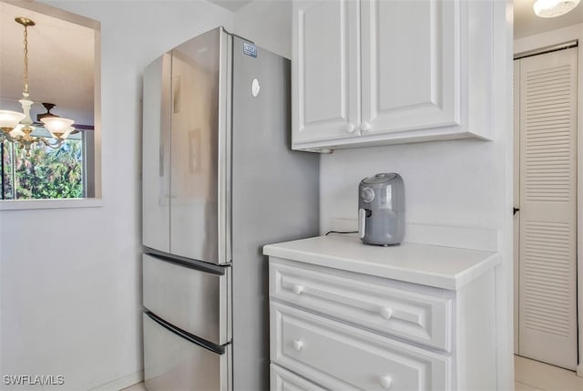 kitchen with an inviting chandelier, white cabinetry, hanging light fixtures, and stainless steel refrigerator