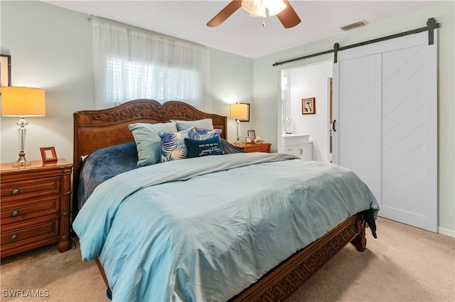 bedroom with a barn door, light colored carpet, ceiling fan, and ensuite bathroom