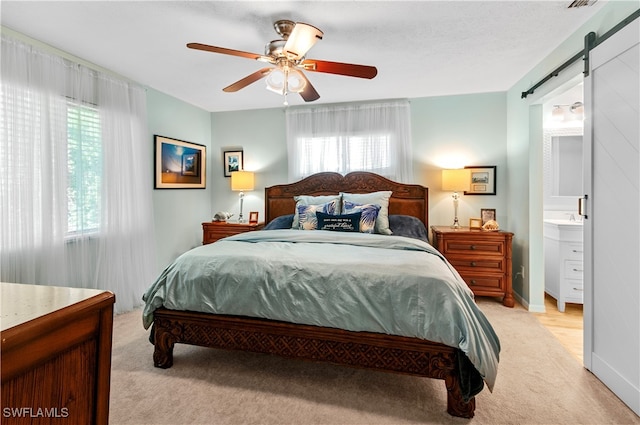 carpeted bedroom with a barn door, ensuite bathroom, ceiling fan, and multiple windows