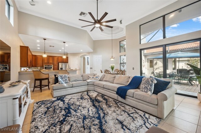 tiled living room with a towering ceiling, ceiling fan, and crown molding