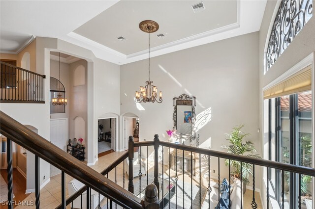 hallway featuring light tile patterned floors, a tray ceiling, an inviting chandelier, and crown molding