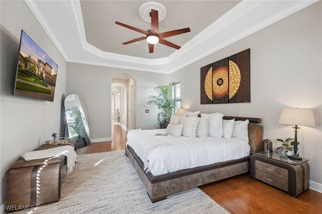 bedroom featuring ceiling fan, wood-type flooring, ornamental molding, and a tray ceiling