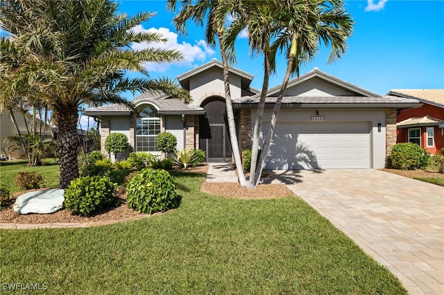 ranch-style home with stucco siding, an attached garage, decorative driveway, a front yard, and brick siding