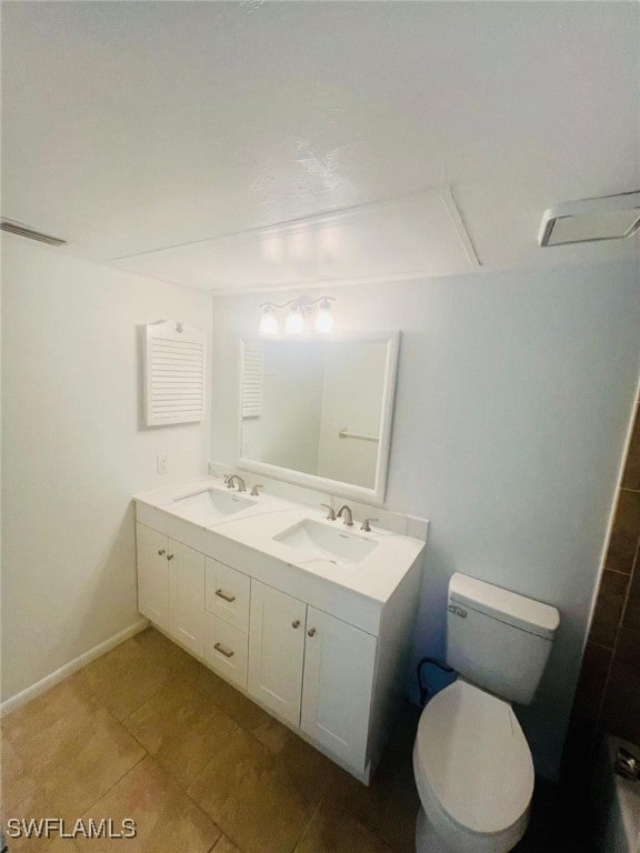 bathroom with double vanity, a sink, toilet, and baseboards