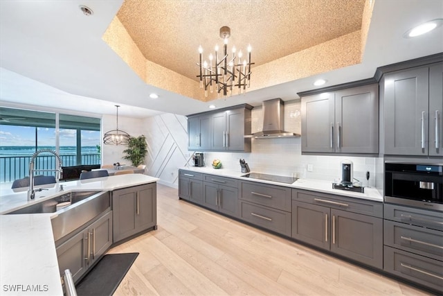 kitchen with black electric stovetop, wall chimney range hood, pendant lighting, and a tray ceiling