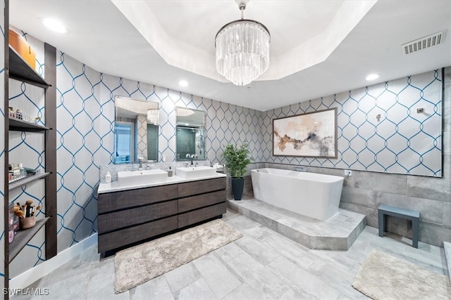 bathroom featuring a chandelier, vanity, a raised ceiling, a bathtub, and tile walls