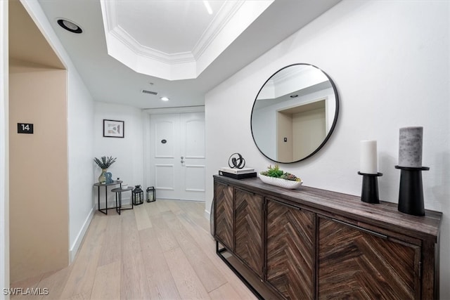 hall featuring ornamental molding, light hardwood / wood-style floors, and a tray ceiling