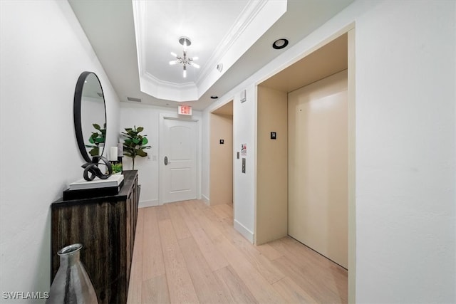 corridor featuring light hardwood / wood-style floors, elevator, ornamental molding, an inviting chandelier, and a tray ceiling