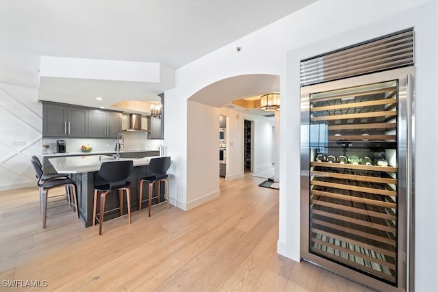 interior space with a kitchen breakfast bar, wall chimney exhaust hood, beverage cooler, and light wood-type flooring