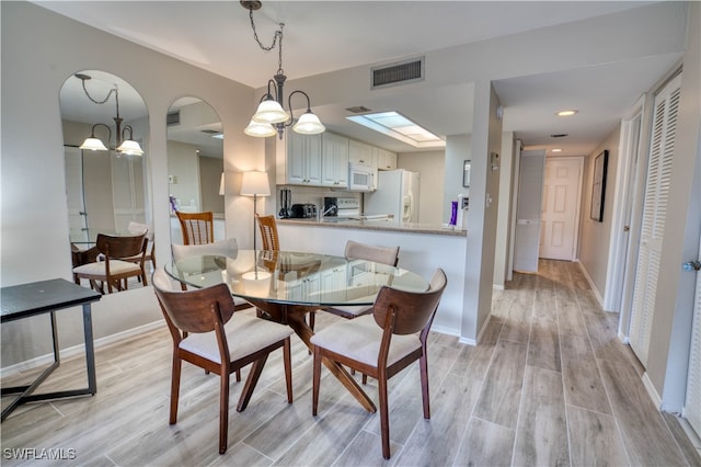 dining room with a skylight, an inviting chandelier, and light hardwood / wood-style floors