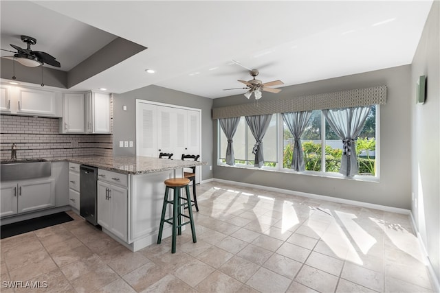 kitchen with kitchen peninsula, a kitchen bar, dark stone counters, sink, and white cabinetry