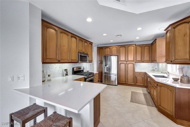 kitchen with kitchen peninsula, tasteful backsplash, a breakfast bar area, appliances with stainless steel finishes, and sink