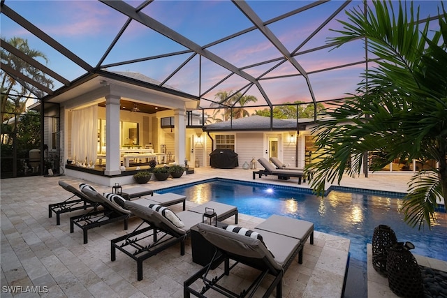 pool at dusk featuring a lanai, a grill, ceiling fan, and a patio