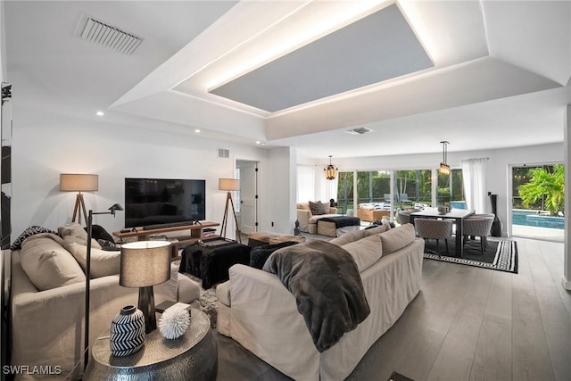 living room featuring a chandelier, wood-type flooring, and a tray ceiling